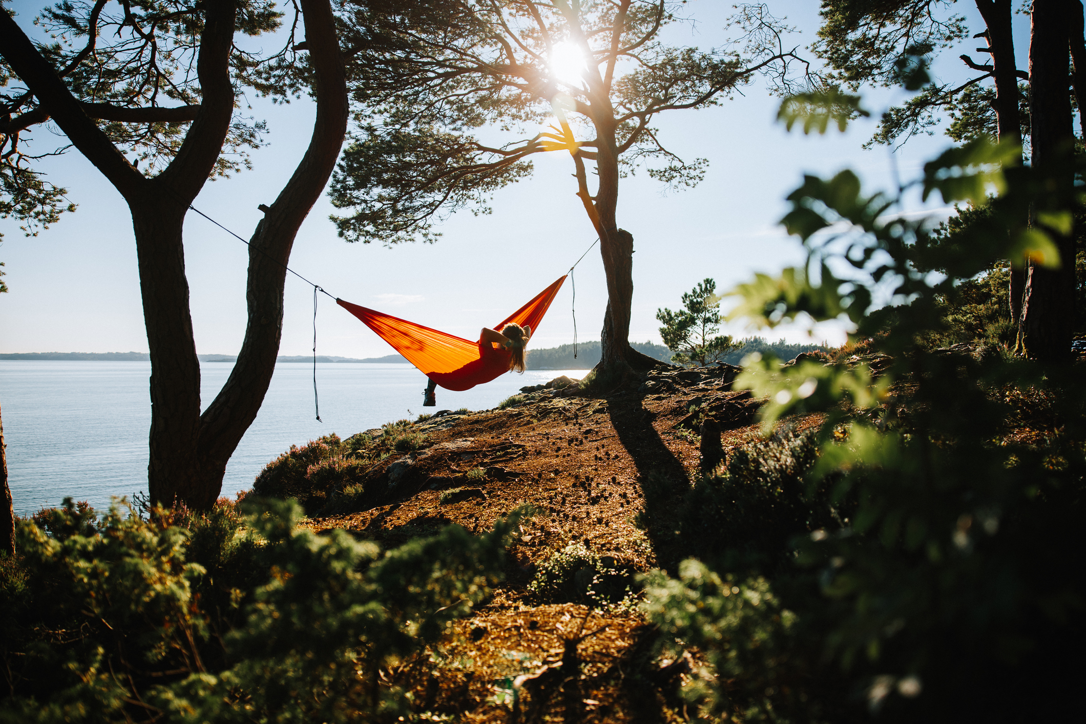 Woman laying in a yellow hammock by a water