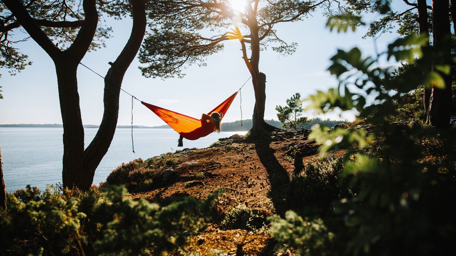 Woman laying in a yellow hammock by a water